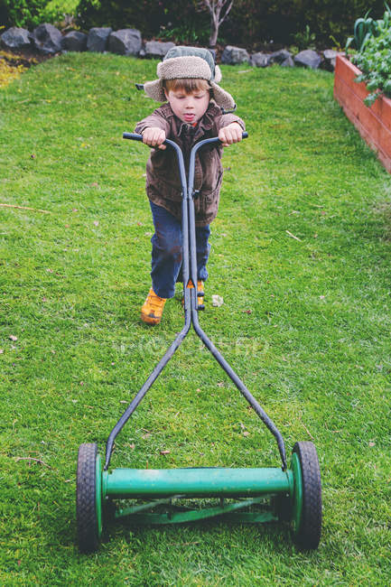 Хлопчик в капелюсі косить газон в саду — стокове фото