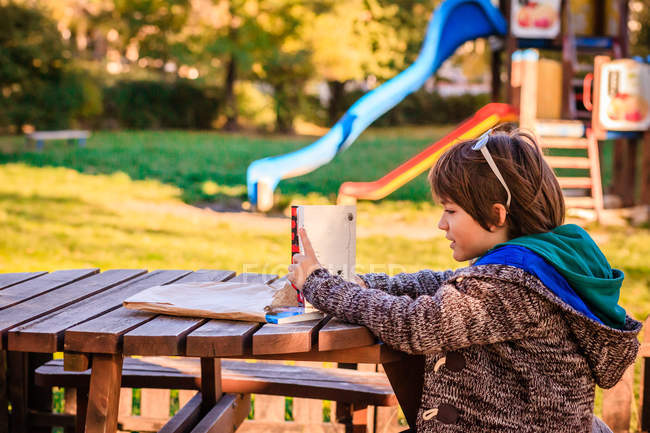 Хлопчик, читаючи книгу в дерев'яний стіл у парку — стокове фото