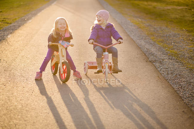 Dos monas hermanas felices montando bicicletas juntas - foto de stock