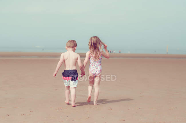 Vista posteriore di Ragazza e ragazzo che si tiene per mano e cammina sulla spiaggia sabbiosa — Foto stock