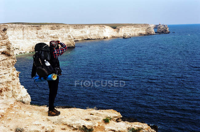 Турист на краю скалы фотографирует море, вид сзади — стоковое фото