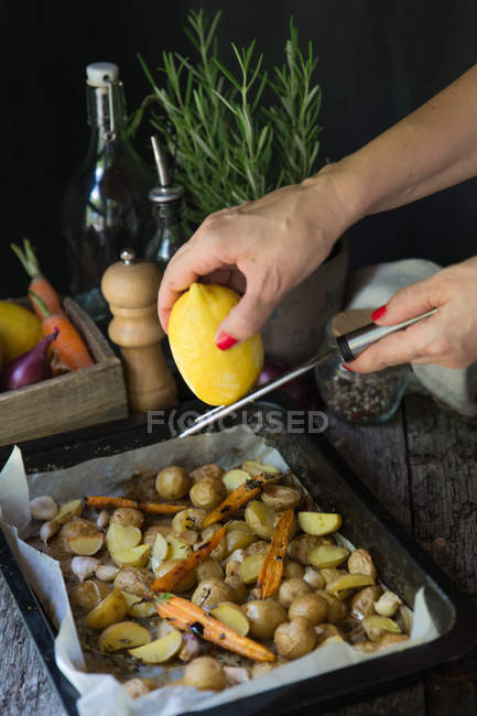 Woman grating lemon over roasted potatoes, garlic and carrots — Stock Photo