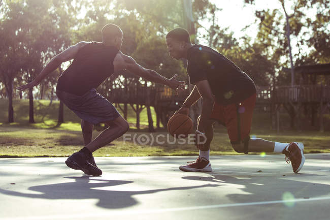 Deux jeunes hommes jouant au basket dans le parc au coucher du soleil — Photo de stock