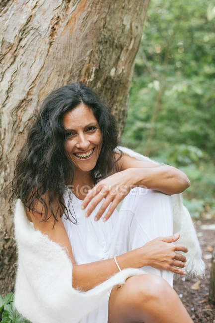 Porträt einer lächelnden Frau, die sich an einen Baum lehnt und in die Kamera blickt — Stockfoto
