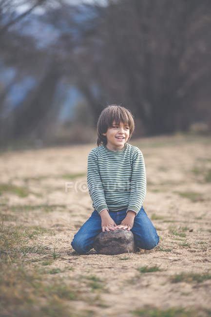 Garçon souriant assis sur un rocher sur le chemin — Photo de stock