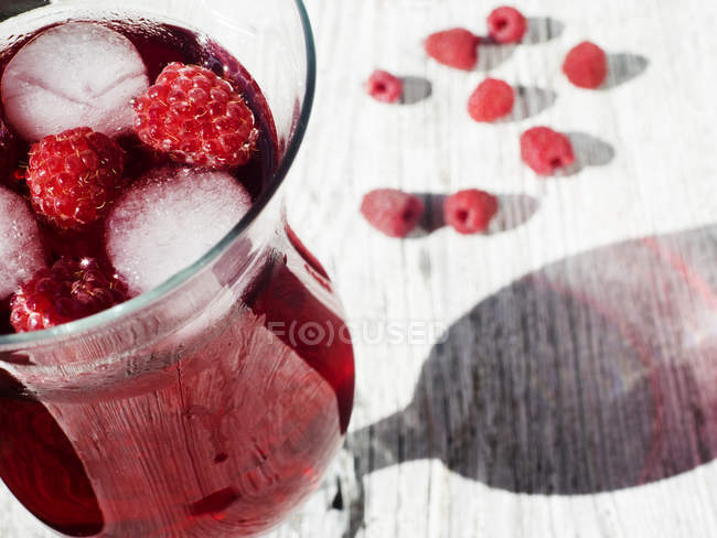 Lemonade glass with raspberry and ice cubes inside on wooden table — Stock Photo