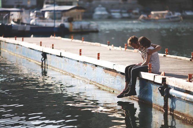 Beautiful teenagers couple sitting and hugging on wooden jetty — Stock Photo