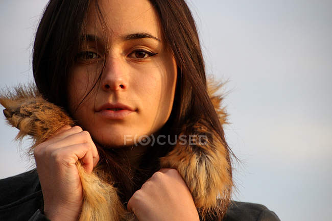 Молодая женщина в теплом пальто с меховым капюшоном смотрит в камеру — стоковое фото