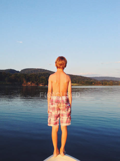 Rückansicht eines Jungen, der auf dem Bug eines Bootes steht, das bereit ist, ins Meer zu springen — Stockfoto