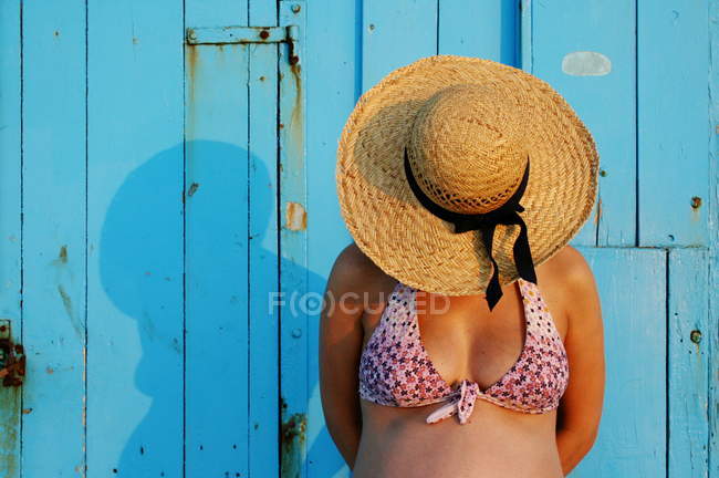 Mujer embarazada con un sombrero de paja de pie delante de la pared azul - foto de stock