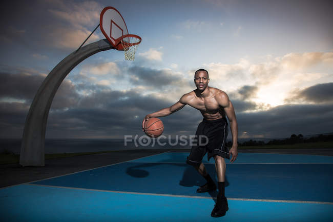 Young man playing basketball in a park with dramatic sky on background — Stock Photo