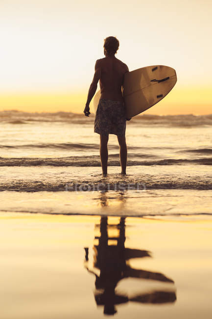 Mann steht am Strand bei Sonnenaufgang mit Surfbrett, San Diego, Kalifornien, Amerika, Vereinigte Staaten — Stockfoto