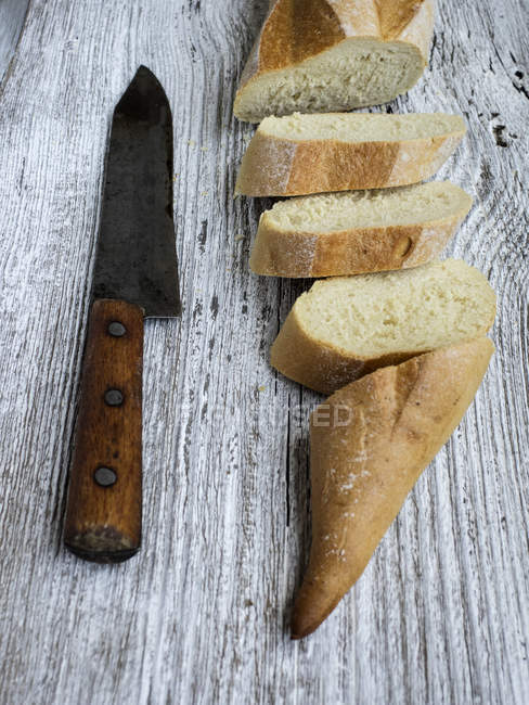 Slices of bread and knife on wooden table, elevated view — Stock Photo