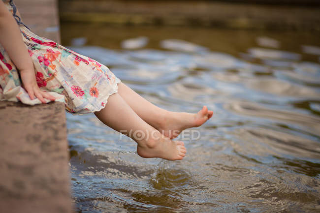 Abgeschnittenes Bild eines Mädchens, das seine Füße in Wasser taucht — Stockfoto