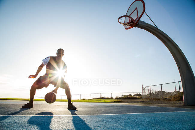 Jeune homme jouant au basket dans un parc en contre-jour — Photo de stock