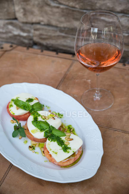 Ensalada de tomate y mozzarella con copa de vino de rosas - foto de stock
