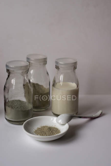 Três frascos com pó e leite contra a parede cinzenta — Fotografia de Stock