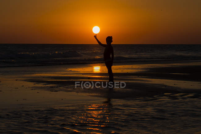 Силуэт мальчика, стоящего на пляже балансируя солнце на пальце — стоковое фото