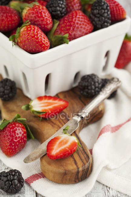 Frische ganze und halbierte Erdbeeren und Brombeeren auf einem hölzernen Schneidebrett — Stockfoto