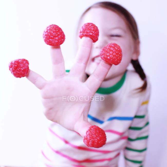Primer plano de Chica mostrando frambuesas en los dedos - foto de stock