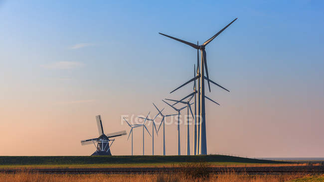 Zeilen von Windkraftanlagen und eine alte traditionelle Windmühle, Eemshaven, Groningen, Niederlande — Stockfoto