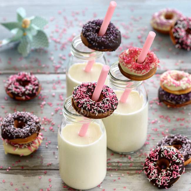 Composition of donuts over straws of bottles of milk at wooden table — Stock Photo