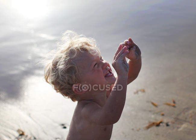 Улыбающийся мальчик держит песчаные руки на пляже — стоковое фото