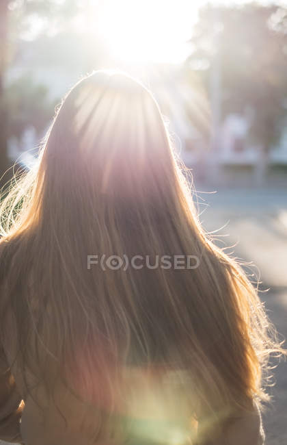 Вид сзади на женщину с длинными волосами, идущую по улице в солнечном свете — стоковое фото