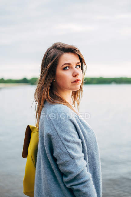 Portrait of woman with yellow backpack standing next to sea — Stock Photo