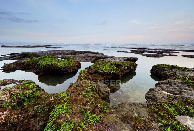 Vista panoramica sulle rocce coperte di muschio al tramonto, Mengening beach, Bali, Indonesia — Foto stock