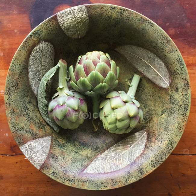 Alcachofas frescas en tazón estampado sobre mesa de madera - foto de stock
