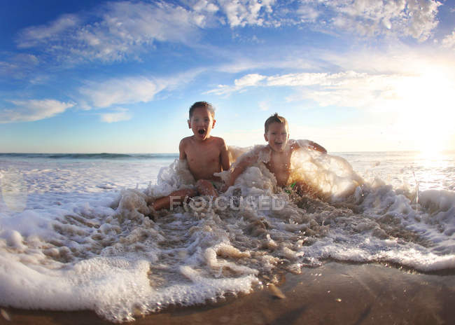 Dos chicos caucásicos divirtiéndose en el agua del océano - foto de stock