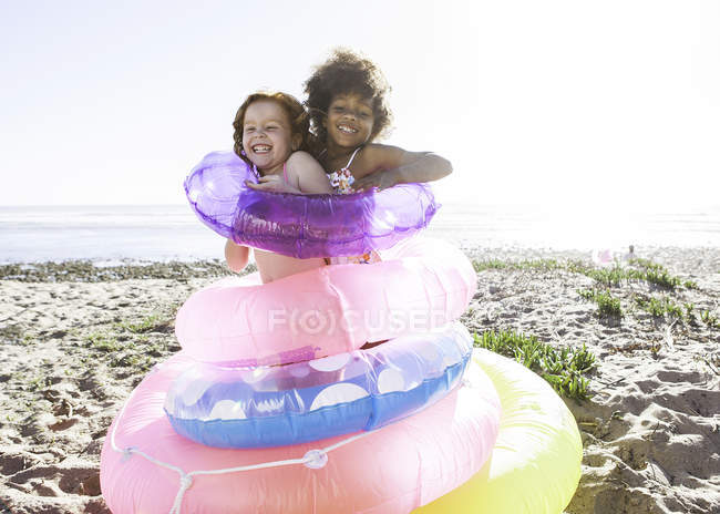Duas meninas bonitos se divertindo com anéis de flutuação na praia — Fotografia de Stock