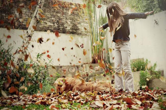 Дівчина і собака грають з осіннім листям в саду — стокове фото