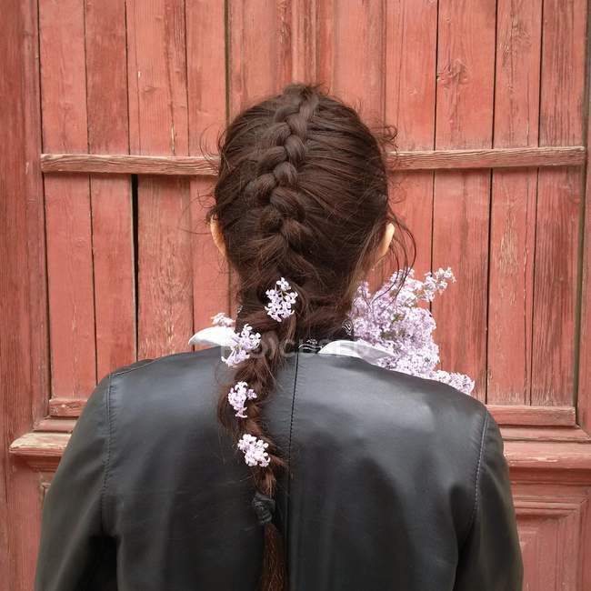 Vue arrière de la fille avec des fleurs lilas dans les cheveux en face du mur en bois brun — Photo de stock