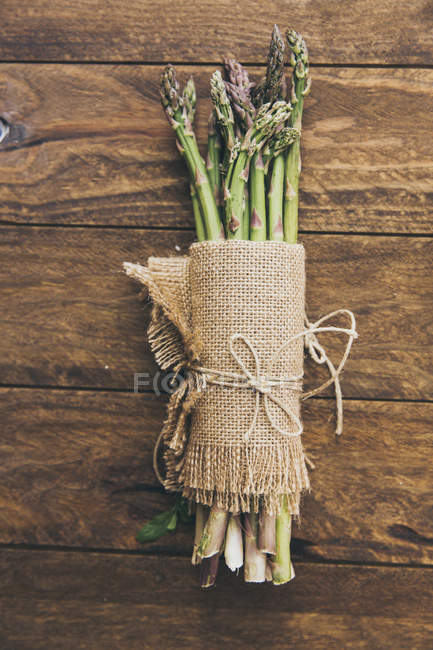 Bunch of fresh asparagus wrapped in linen cloth on wooden table — Stock Photo