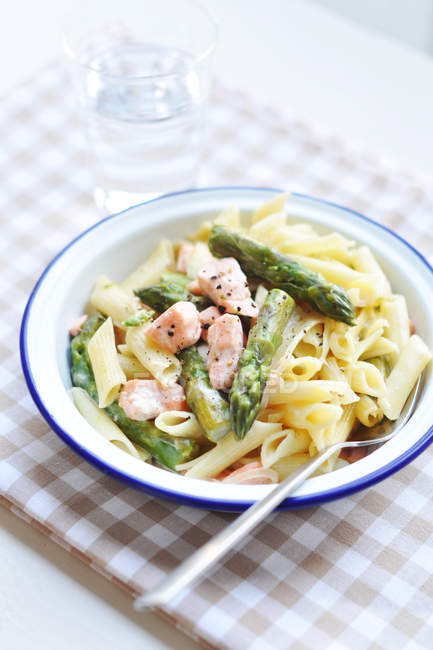 Bowl of Asparagus and Salmon pasta with glass of water — Stock Photo