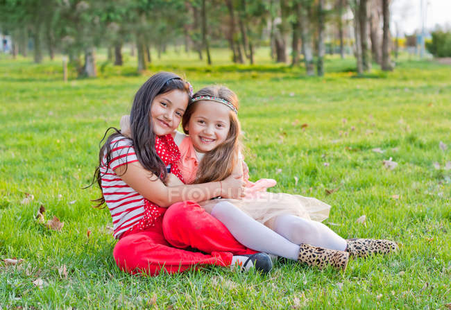 Две маленькие кавказские девочки обнимаются на траве в парке — стоковое фото