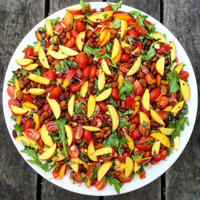 Salada com tomate, pêssegos e manjericão em prato branco — Fotografia de Stock
