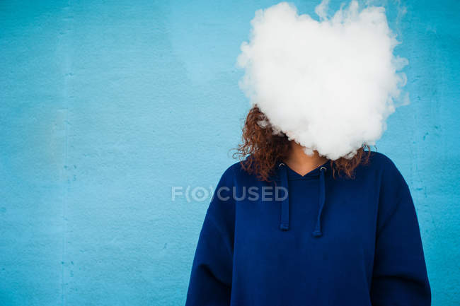 Mujer joven con la cabeza en la nube de humo de vapor sobre fondo azul - foto de stock