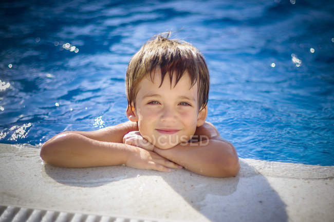 Retrato de menino sorridente inclinado na borda de uma piscina — Fotografia de Stock