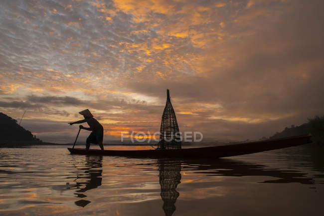 Silhueta de um homem que pesca no lago ao pôr-do-sol, Tailândia — Fotografia de Stock