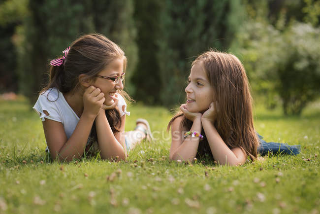 Two Cute Teenage Girls Lying On Green Grass And Looking At Each Other Stock Photo Two Cute Teenage Girls Lying On Green Grass And Looking At Each Other Stock Photo