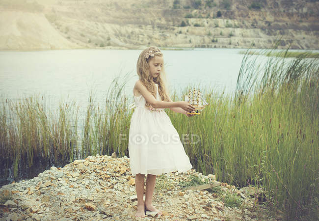 Chica de pie junto a un lago y sosteniendo el modelo de un barco - foto de stock