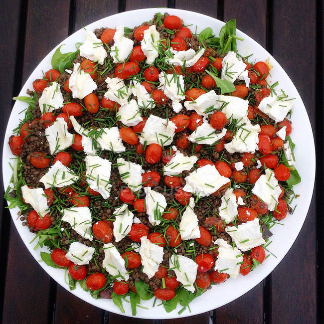 Салат с чечевицей, помидорами и козьим сыром в белой тарелке, вид сверху — стоковое фото