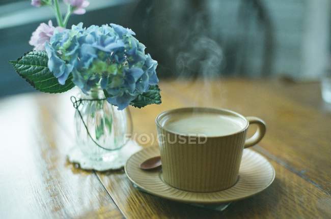 Cup of coffee next to a vase of hydrangeas — Stock Photo