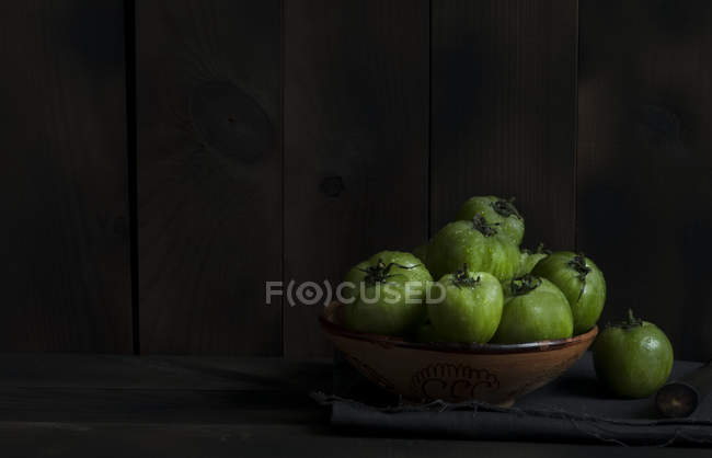 Зеленые помидоры в миске на столе на темном фоне — стоковое фото