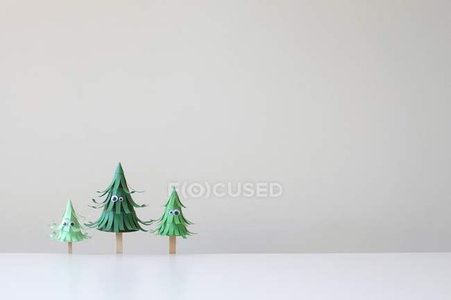 Trois arbres artisanaux en papier avec les yeux contre le mur blanc — Photo de stock