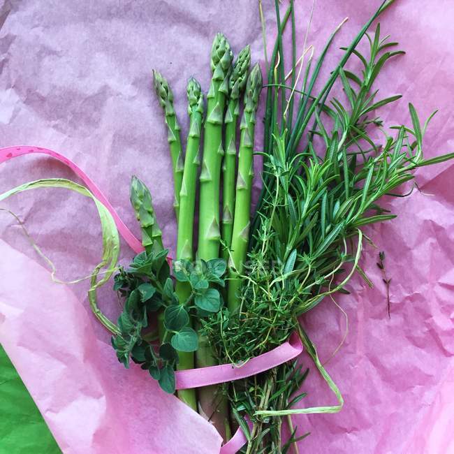 Asparagus and herbs on pink tissue paper — Stock Photo