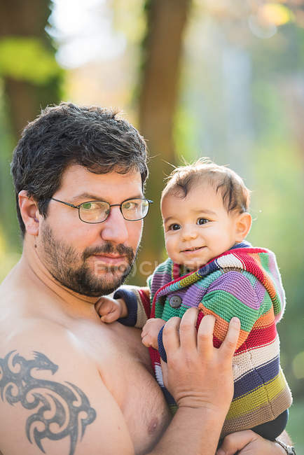 Портрет людини з окулярами та татуюванням, що тримає маленького хлопчика на руках — стокове фото